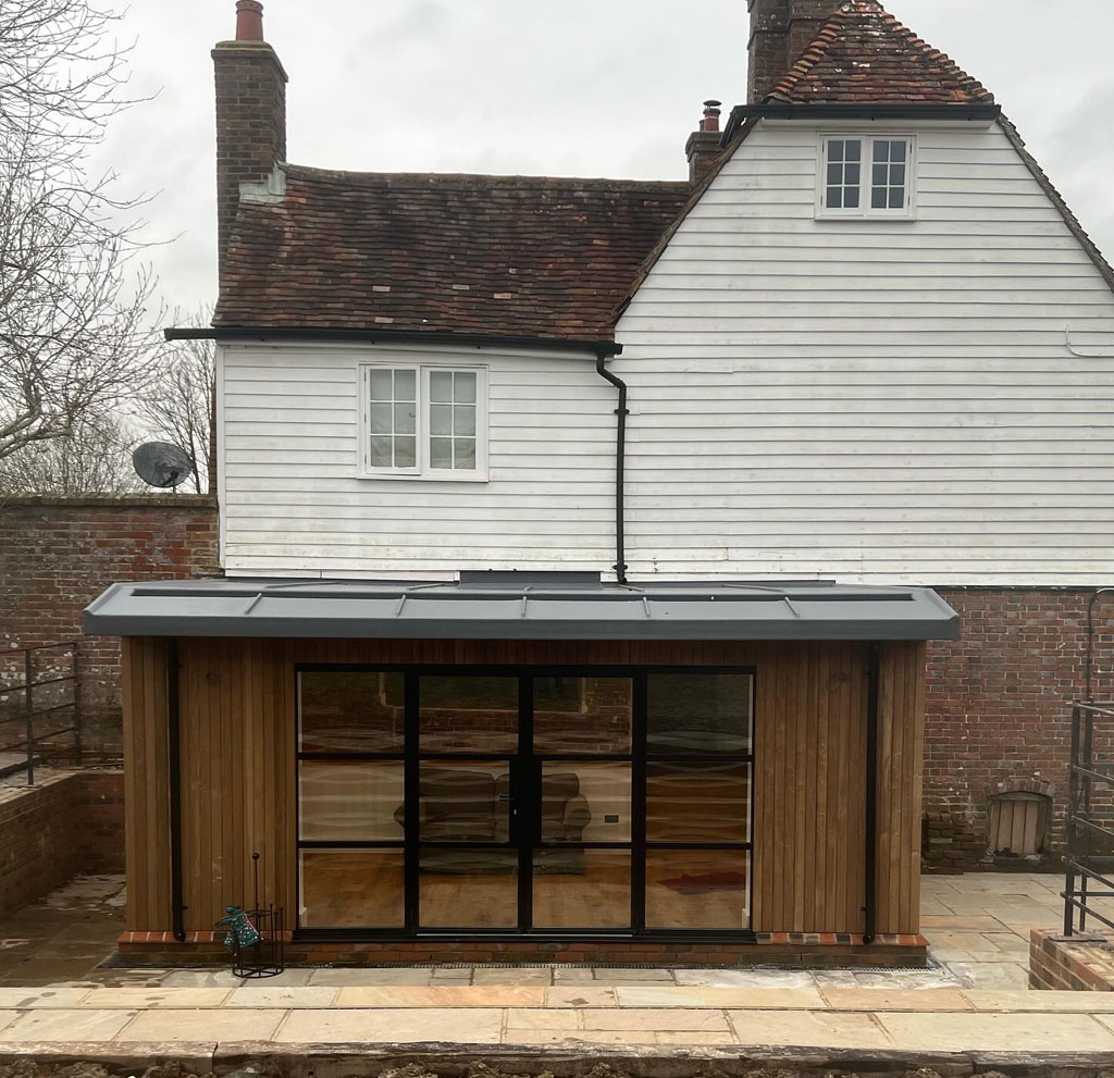 Finished timber clad garden room with black framed glazing at the back of a weatherboarded and brick house
