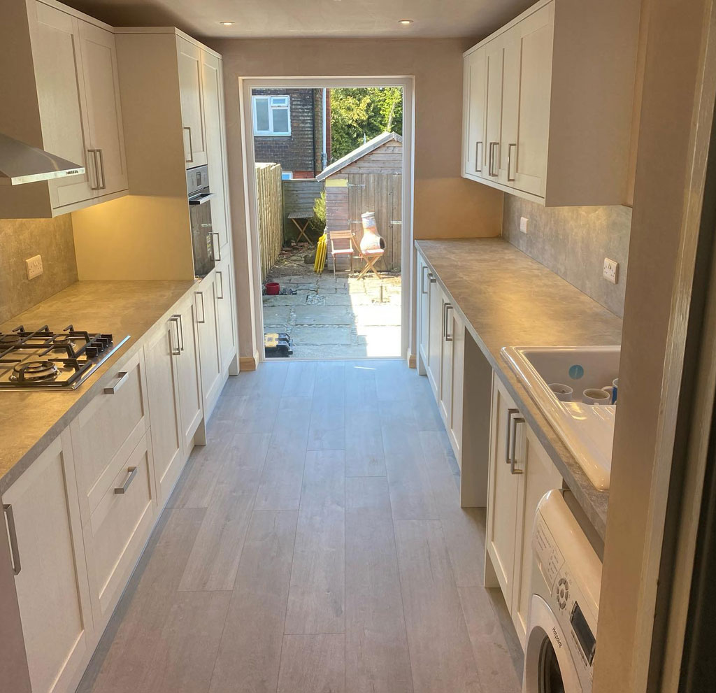 Cream shaker style galley kitchen with wood effect flooring and a door to the garden